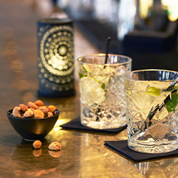 Drinks resting on cocktail napkins on a bar surface with snacks