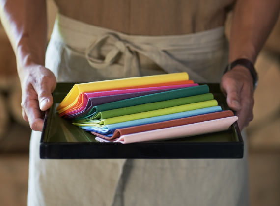 A waiter holding a tray. On the tray are displayed Duni's new Bio Dunisoft napkins. Each one has a different colour.